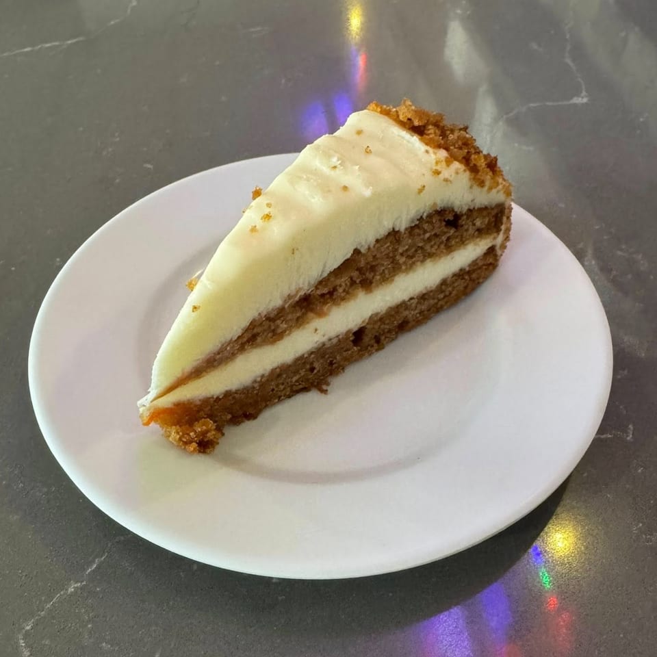 A slice of carrot cake with white cream cheese frosting on a white plate.