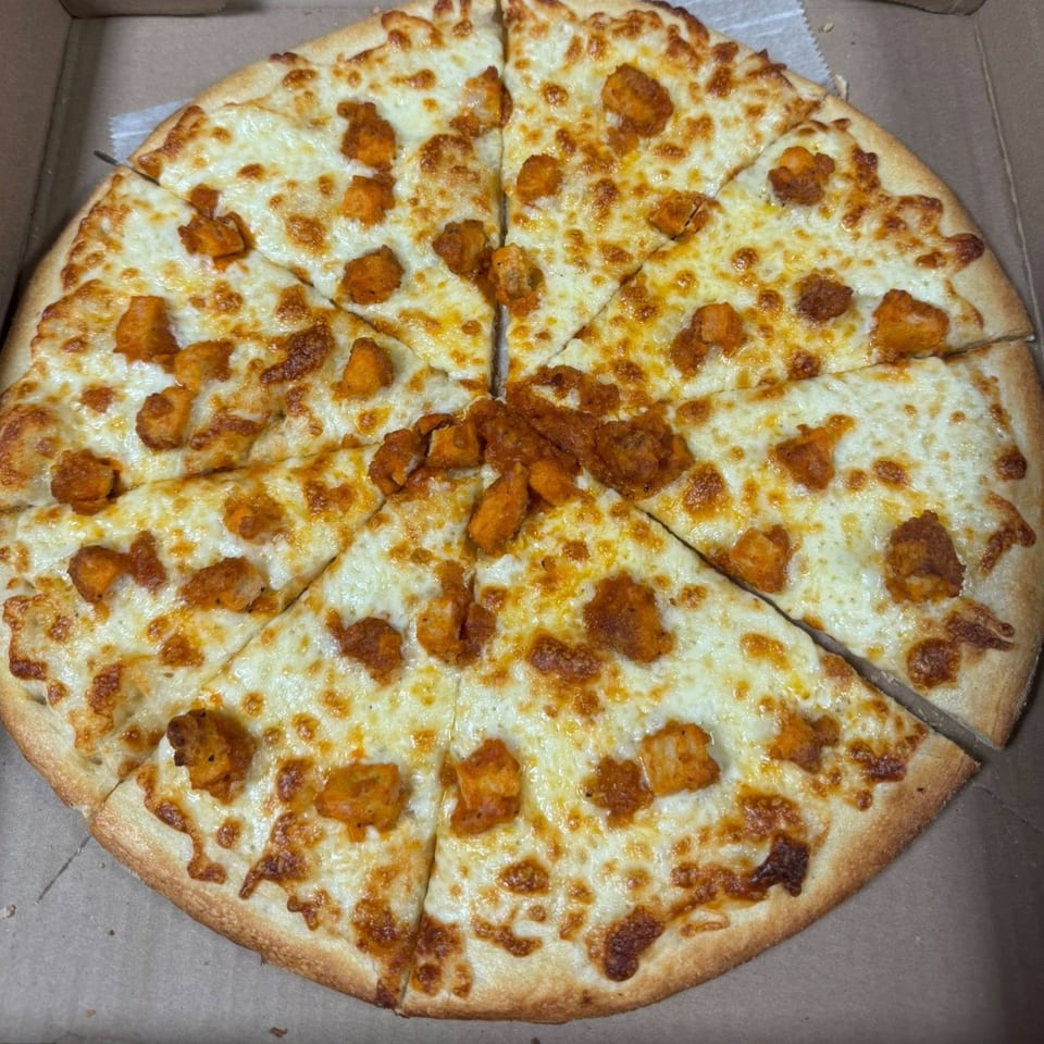 A Falcon Pizza West Haven buffalo chicken pizza, cut into eight slices, in a cardboard box.