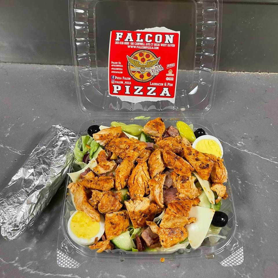 A Falcon Pizza chicken salad with hard-boiled eggs, olives, and cheese in a plastic container.