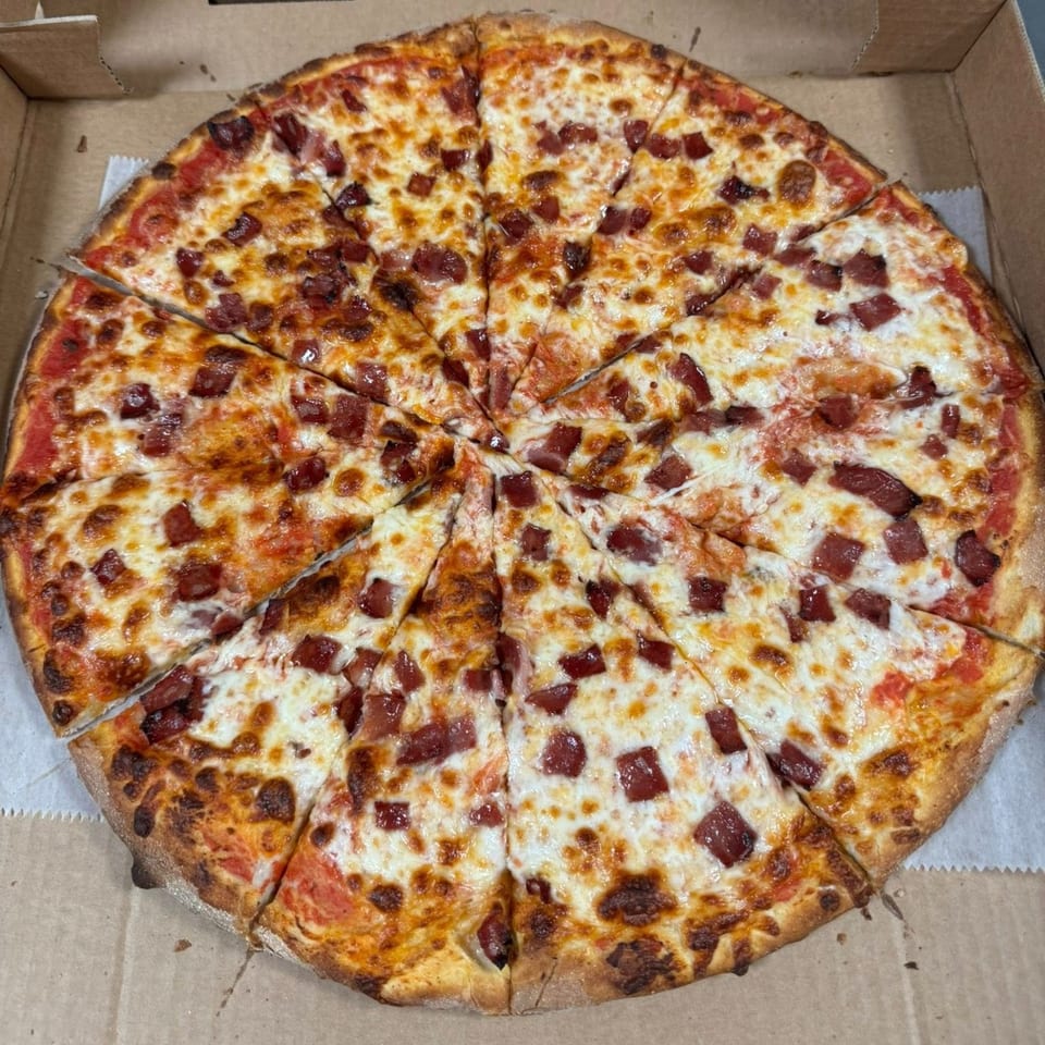 A whole Falcon Pizza with melted cheese and diced pepperoni, sliced and ready to eat in a box.
