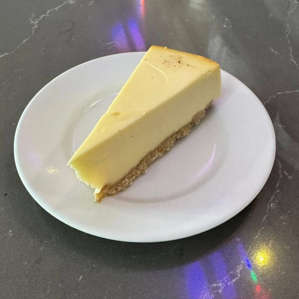 A slice of classic cheesecake with a graham cracker crust on a white plate.
