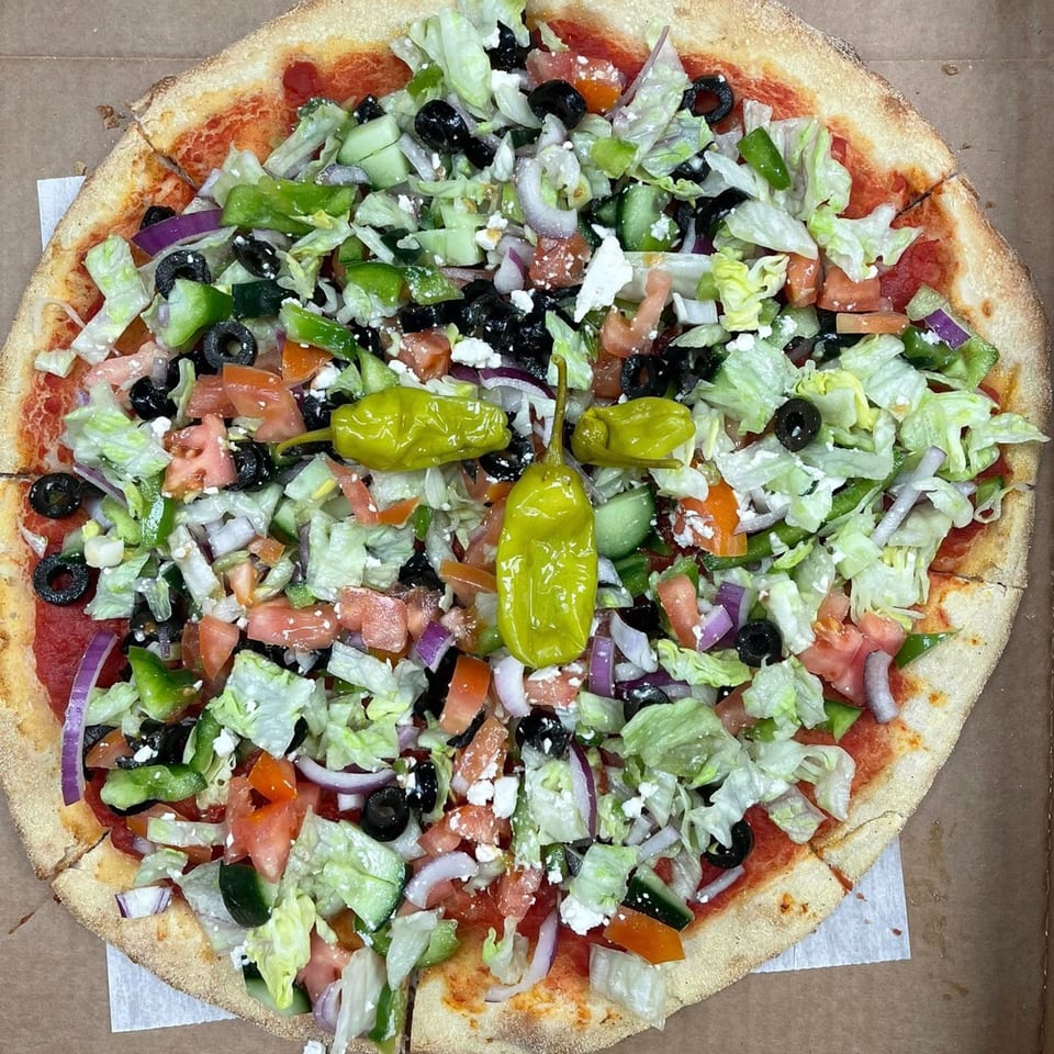 A Falcon Pizza West Haven pizza topped with fresh salad, olives, and peppers.
